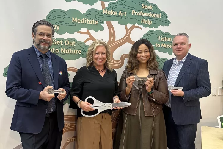 Two men and two women with oversized scissors and ceremonial keys standing in front of a wall mural of a tree with mental…