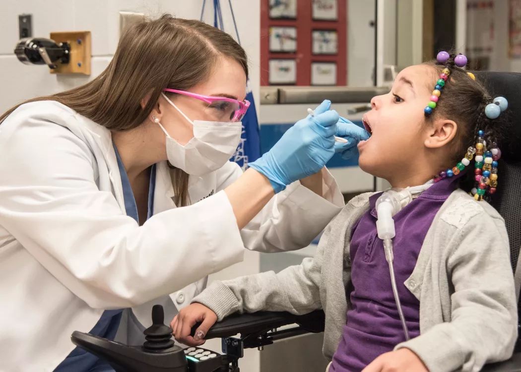 Elementary student opens her mouth for a dental student to give her an exam.
