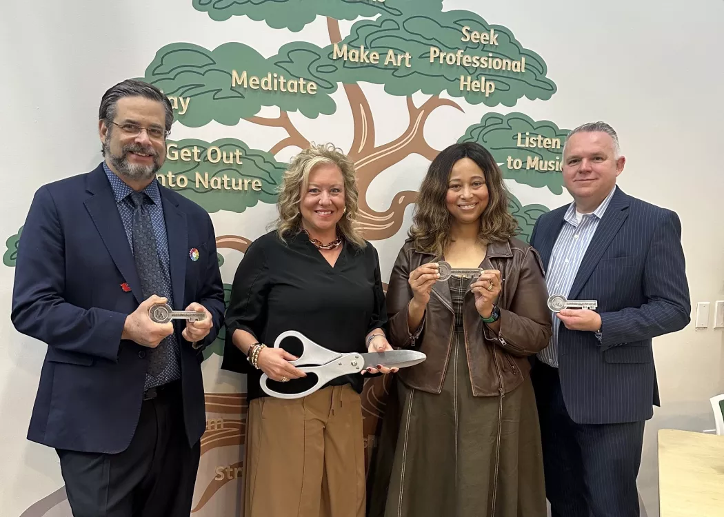 Two men and two women with oversized scissors and ceremonial keys standing in front of a wall mural of a tree with mental…