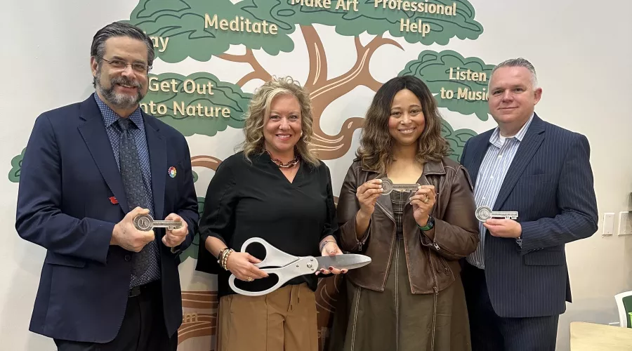 Two men and two women with oversized scissors and ceremonial keys standing in front of a wall mural of a tree with mental…